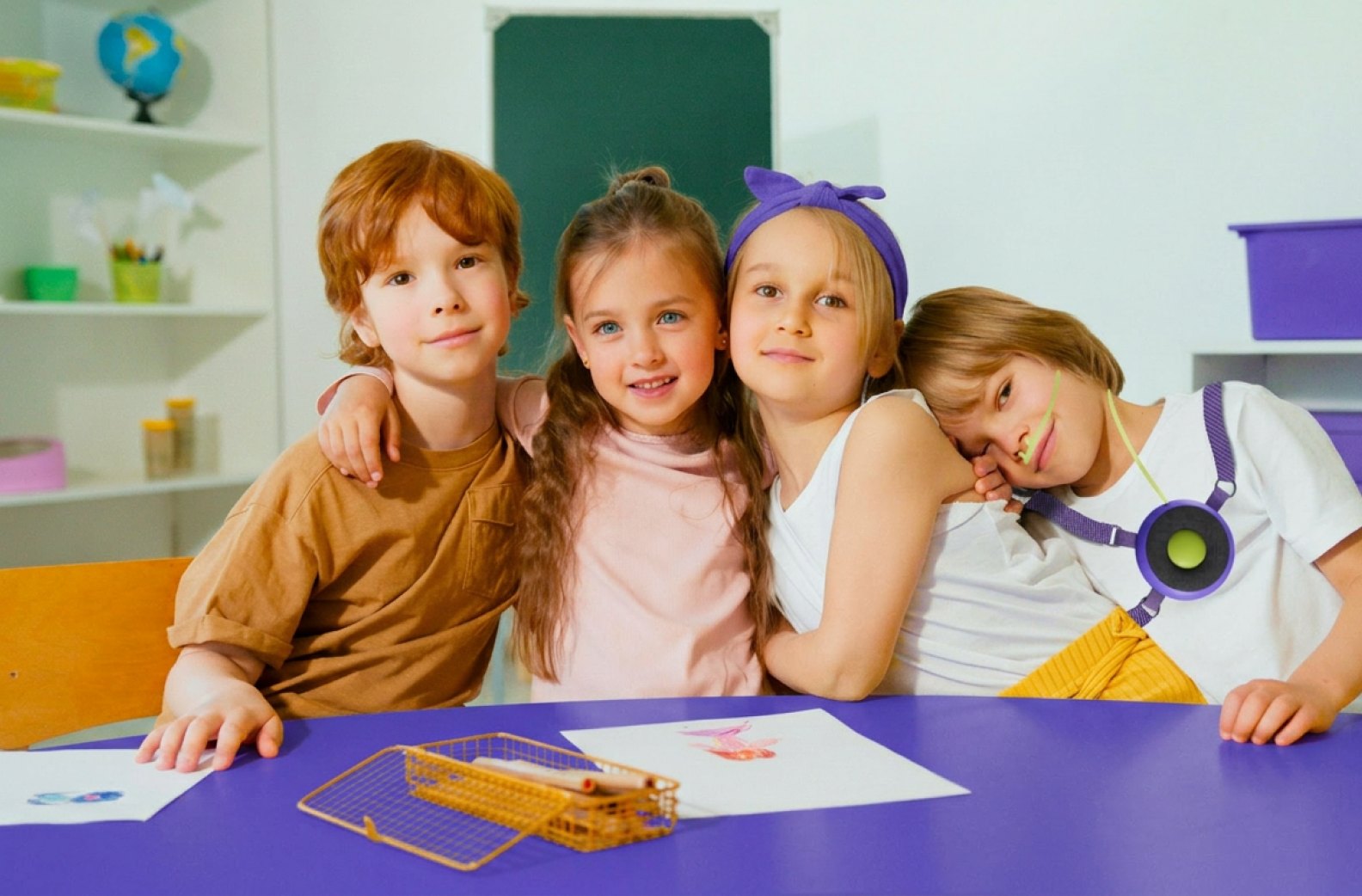 Four children at a classroom table, one wearing Oxi